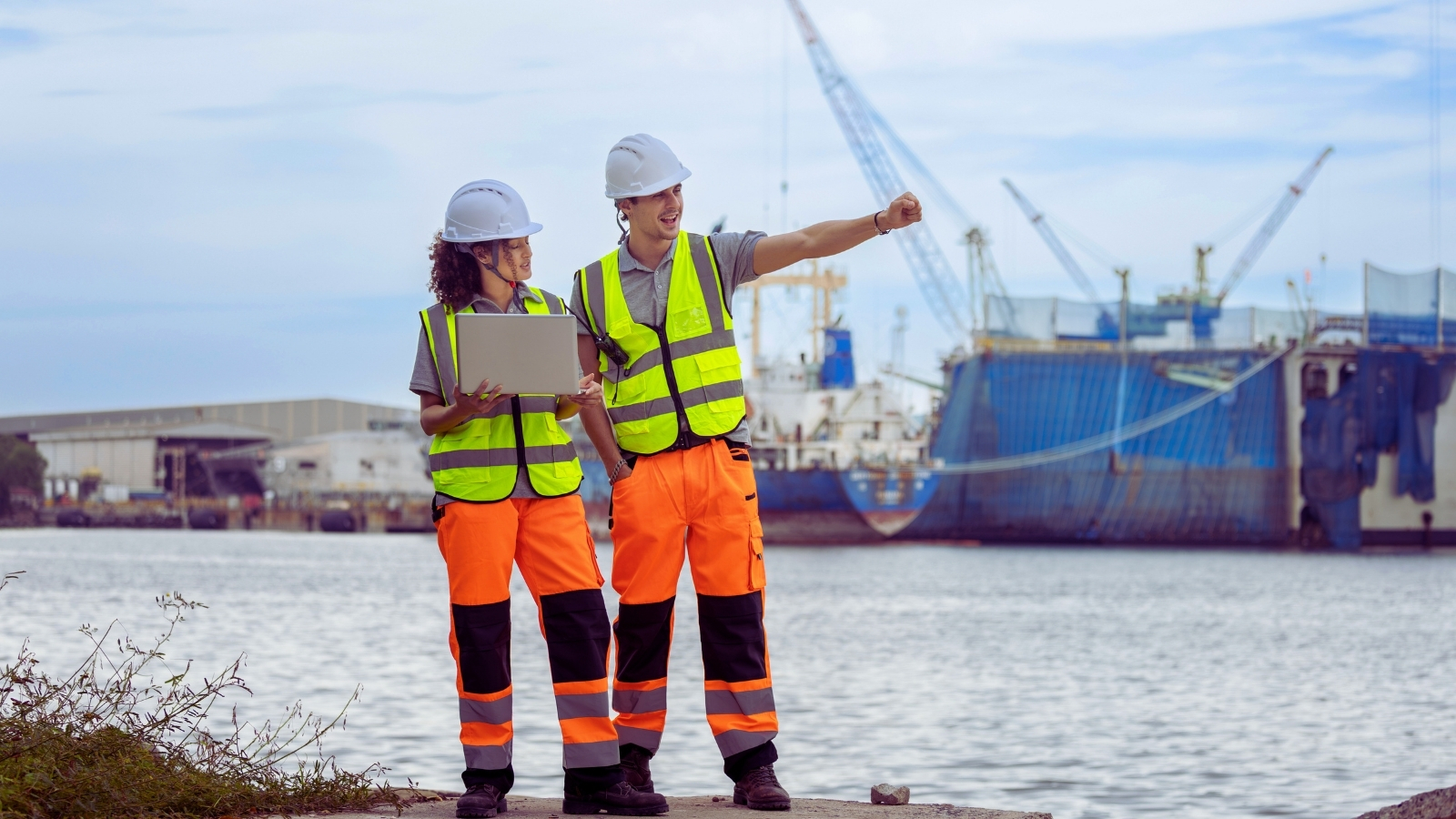 Two engineers in hard hats and hi-vis reviewing a harbour works site from the quay.